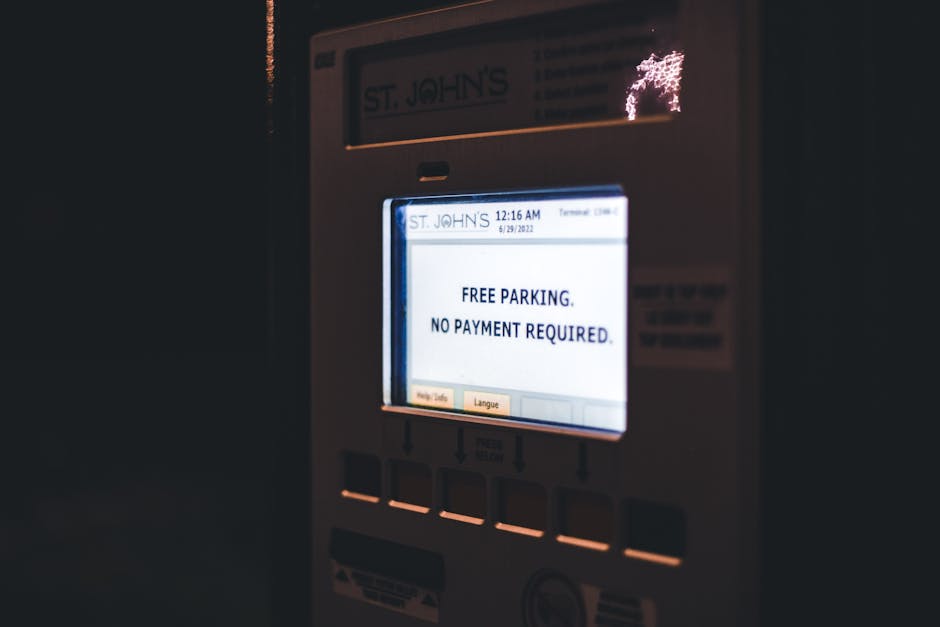 Close-up of an electronic parking meter displaying the message 'FREE PARKING. NO PAYMENT REQUIRED.' The meter is situated outdoors near a curb, with a small part of a building or pavement visible in the background. The screen is illuminated, showing the time as 12:16 AM and the date as June 29, 2022. The device has several buttons below the display, and a portion of the payment slot can be seen at the bottom. The scene reflects a parking payment system that does not require fee payment in this area, which can be relevant during a home relocation or furniture transport when parking arrangements are considered, and parking suspensions and fines may be part of the moving logistics managed by professionals like Man with Van St Margarets.